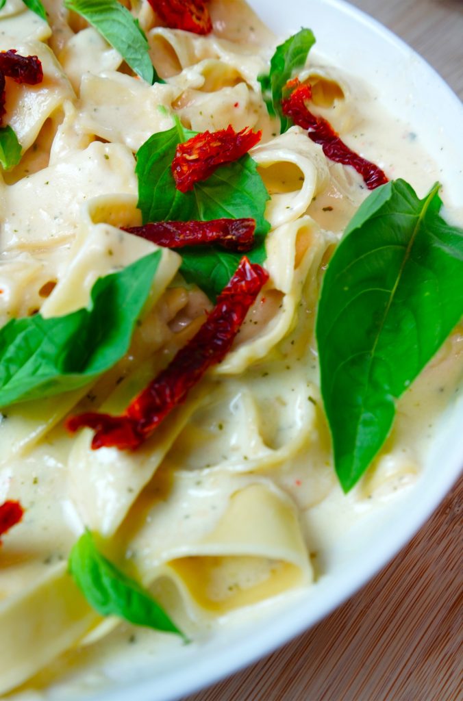 delicious plate of creamy alfredo sauce on top of spiced noodles, basil and dried tomato slices